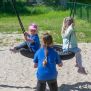 Children playing on a Single Swing (BNS 90cm) with a round netted seat in a sandy playground.